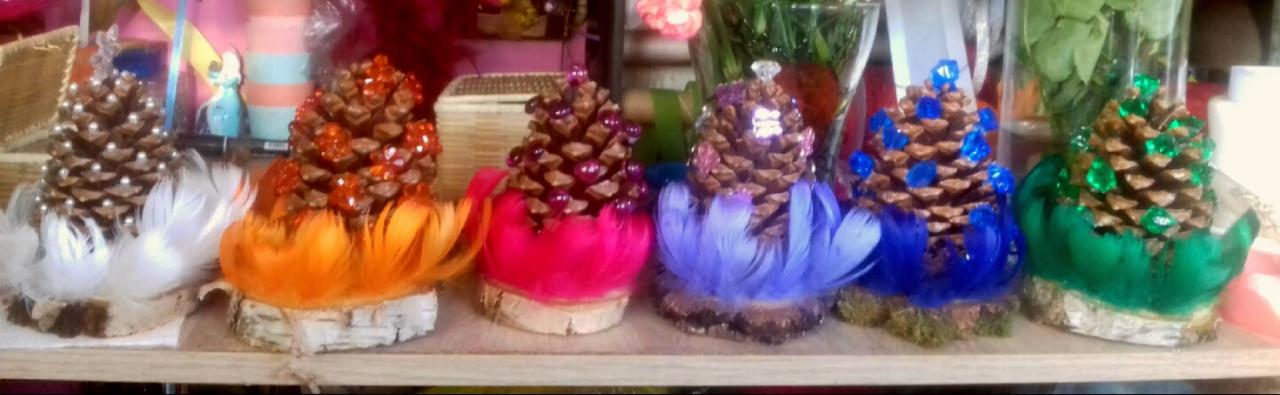 Ręcznie robione ozdoby świąteczne: szyszki pomalowane na brązowo z kolorowymi klejnotami i piórami na drewnianych podstawkach, białe, pomarańczowe, różowe, fioletowe, niebieskie i zielone