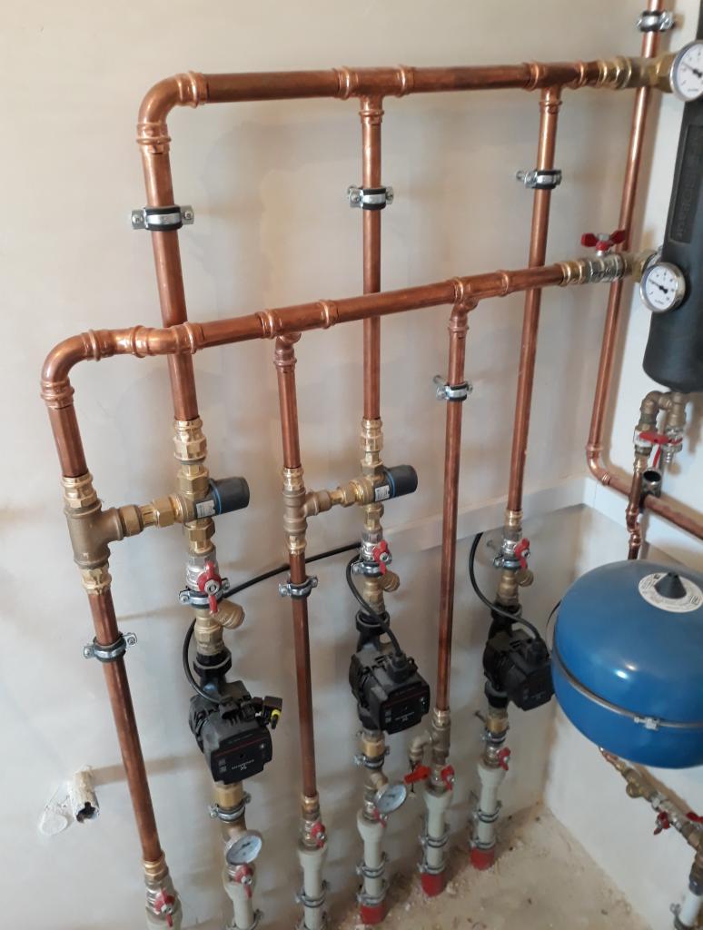 Instalacja centralnego ogrzewania z miedzianymi rurami, pompami obiegowymi i manometrami, zamocowana do ściany w surowym stanie.