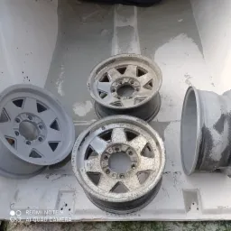 Przygotowanie felg samochodowych do obróbki: trzy felgi przed i jedna po nałożeniu podkładu, widoczne napisy 'OFF ROAD' i '7JX15H2'.