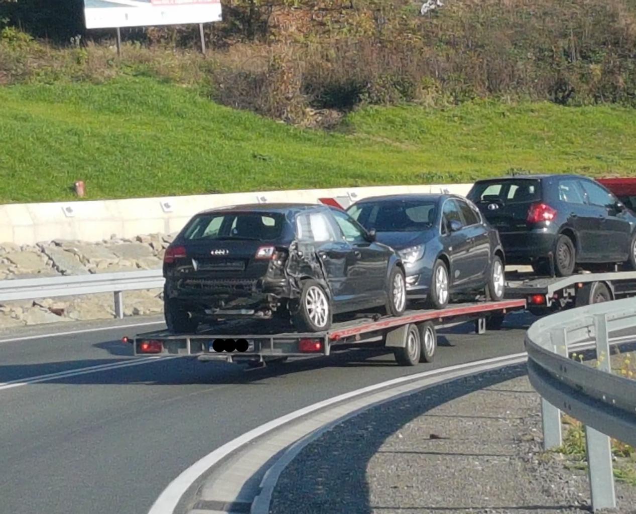 Uszkodzone Audi A3 na lawecie, za nim dwa inne samochody, widok z tyłu na autostradzie.