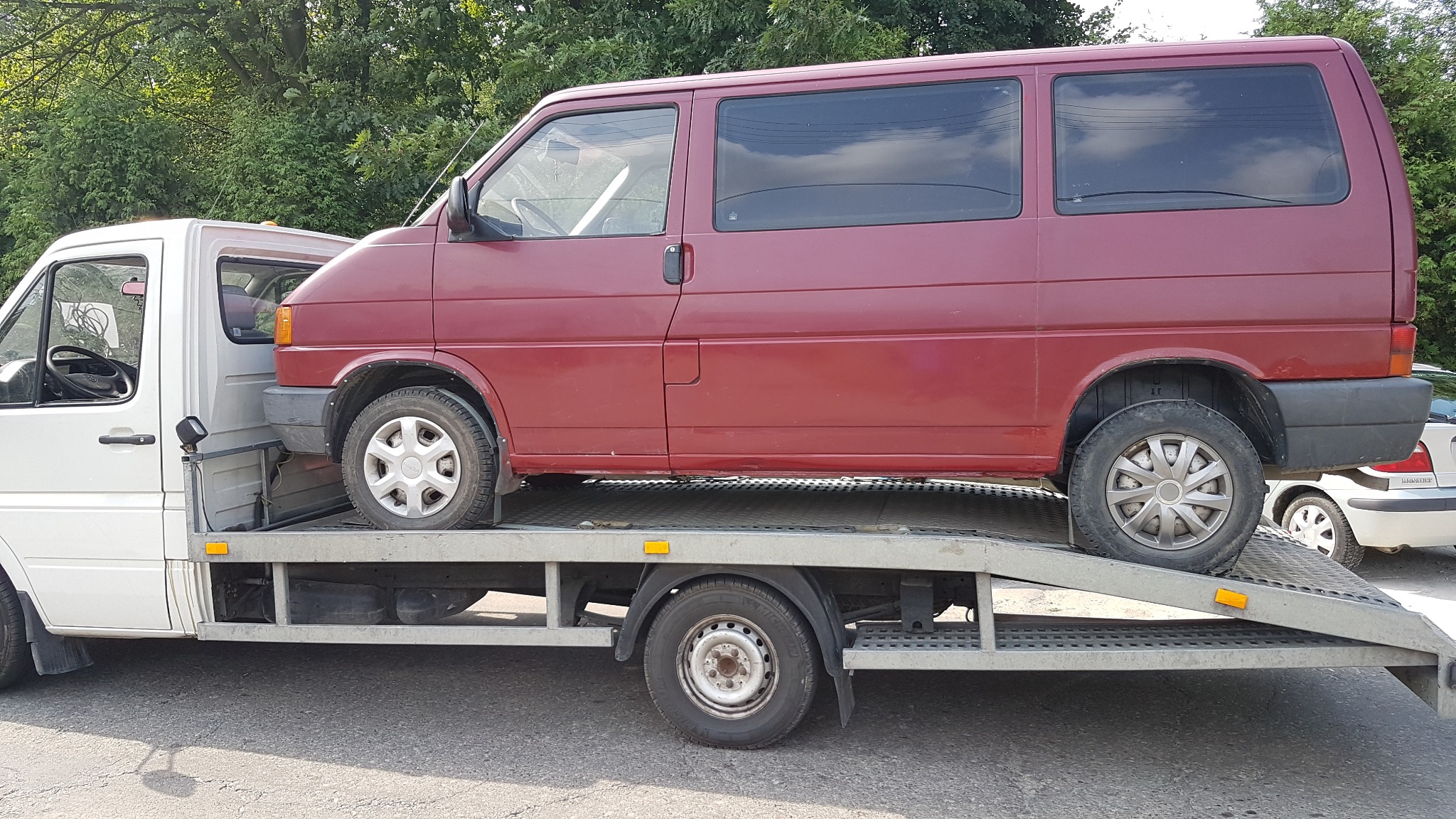 Czerwony bus na platformie lawety, widok z boku, zarys drzew w tle, pojazd zabezpieczony przed transportem.