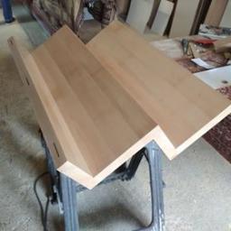 Js Kama - Fragment drewnianych schodów w trakcie montażu, widoczne połączenia kołkowe, na tle warsztatu z dywanem i narzędziami.