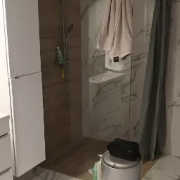 Nowoczesna łazienka z kabiną prysznicową typu walk-in, marmurowymi płytkami na ścianach i podłodze, białymi szafkami, deszczownicą i ręcznikami.