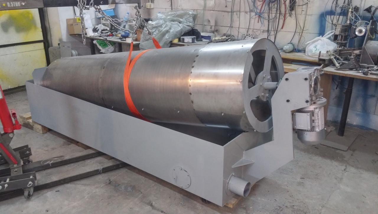 Metalowy, cylindryczny bęben przemysłowy z silnikiem, zabezpieczony pomarańczowym pasem transportowym, umieszczony na szarej, metalowej podstawie, w warsztatowym otoczeniu.