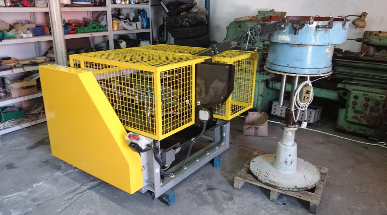 Żółta obudowa zabezpieczająca automat do bram, widoczne elementy sterujące, tło warsztatowe z maszynami.