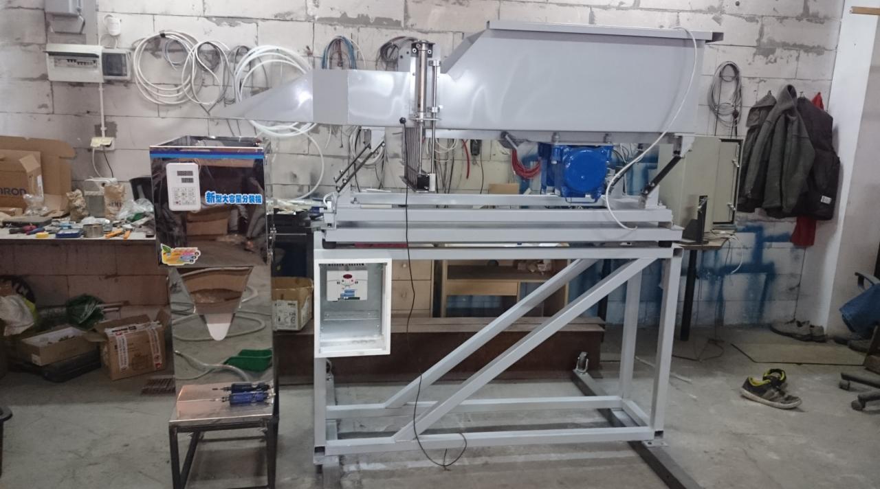 Zdjęcie przedstawia szarą, metalową konstrukcję z niebieskim silnikiem, prawdopodobnie element linii produkcyjnej lub maszyny przemysłowej, w tle widoczne narzędzia i akcesoria w warsztacie.