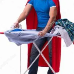 Mężczyzna w niebieskiej koszulce i czerwonej pelerynie prasuje koszulę na desce do prasowania, z boku leży sterta ubrań.