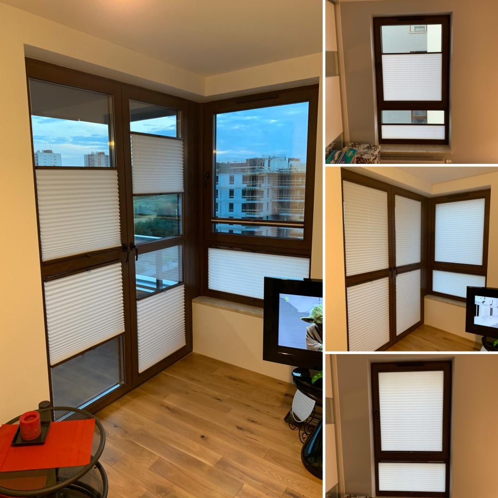 Nowoczesne, plisowane osłony okienne w brązowych ramach zamontowane w narożnym oknie z widokiem na budowę, uzupełnione o mały stolik kawowy z czerwoną dekoracją.