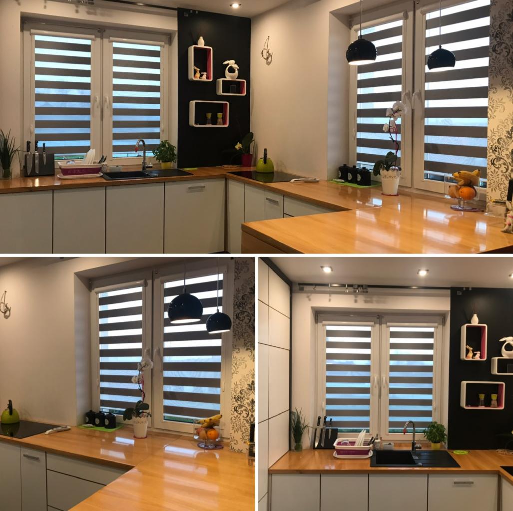Nowoczesna kuchnia z jasnymi szafkami i drewnianym blatem, okno przesłonięte roletami z poziomymi pasami, czarne lampy wiszące i dekoracyjne półki na ścianie.