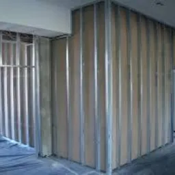 Konstrukcja szkieletowa ścian działowych z profili metalowych i płyt kartonowo-gipsowych w trakcie montażu, widoczne profile pionowe i płyty bazowe, podłoga zabezpieczona folią.