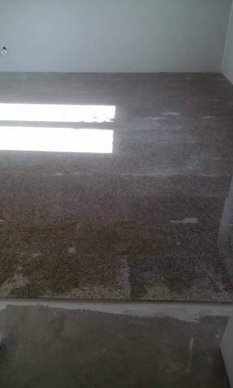 Świeżo położona, błyszcząca, ciemna terakota na podłodze w pomieszczeniu w trakcie prac wykończeniowych, z widocznymi refleksami światła i fragmentem surowej, nie wykończonej podłogi przy ścianie.