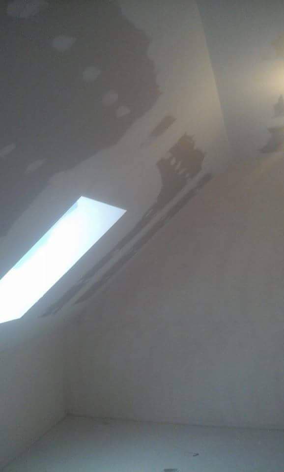 Ściana i sufit w trakcie szpachlowania z widocznym oknem dachowym, nierówności i ślady po szpachli. Oświetlenie górne podkreśla niedoskonałości powierzchni.