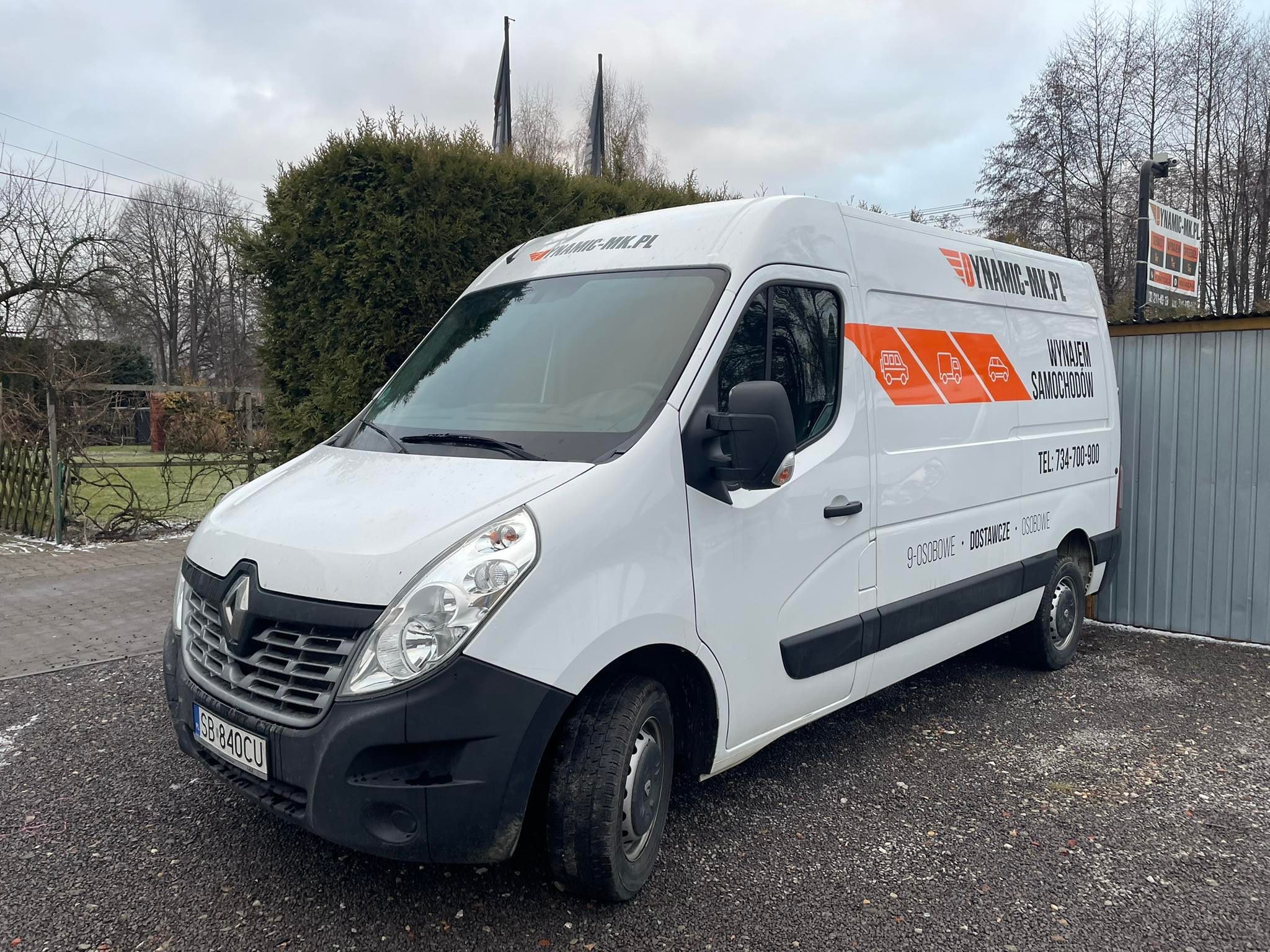 Biały samochód dostawczy Renault Master z pomarańczowym logo firmy Dynamic-Mix.pl oferującej wynajem samochodów osobowych i dostawczych, zaparkowany na żwirowym podłożu.