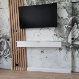 Nowoczesny salon z telewizorem na ścianie z dekoracyjną tapetą w kwiaty, drewnianymi lamelami i białą szafką RTV.