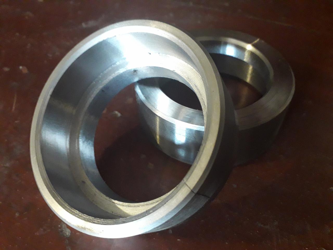 Dwa metalowe pierścienie z widocznymi śladami obróbki na ciemnym, drewnianym tle.