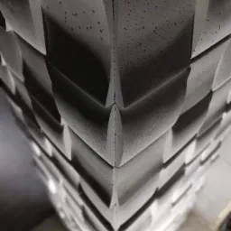 Dekoracyjny panel ścienny z betonu architektonicznego o geometrycznym wzorze, oświetlony od dołu, z widoczną strukturą i porowatością materiału.