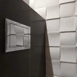 Nowoczesna łazienka z czarną, błyszczącą ścianą i chromowanym przyciskiem spłuczki oraz trójwymiarową, białą ścianą z małymi, ciemnymi plamkami.