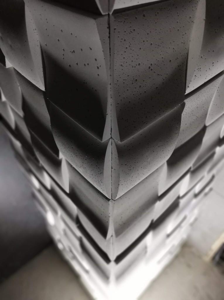 Dekoracyjny panel ścienny z betonu architektonicznego o geometrycznym wzorze, oświetlony od dołu, z widoczną strukturą i porowatością materiału.