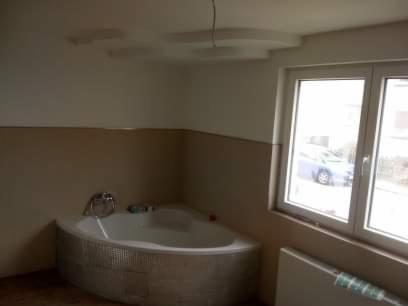 Narożna wanna z hydromasażem obłożona mozaiką w łazience z beżowymi ścianami i oknem z widokiem na zaparkowany samochód.