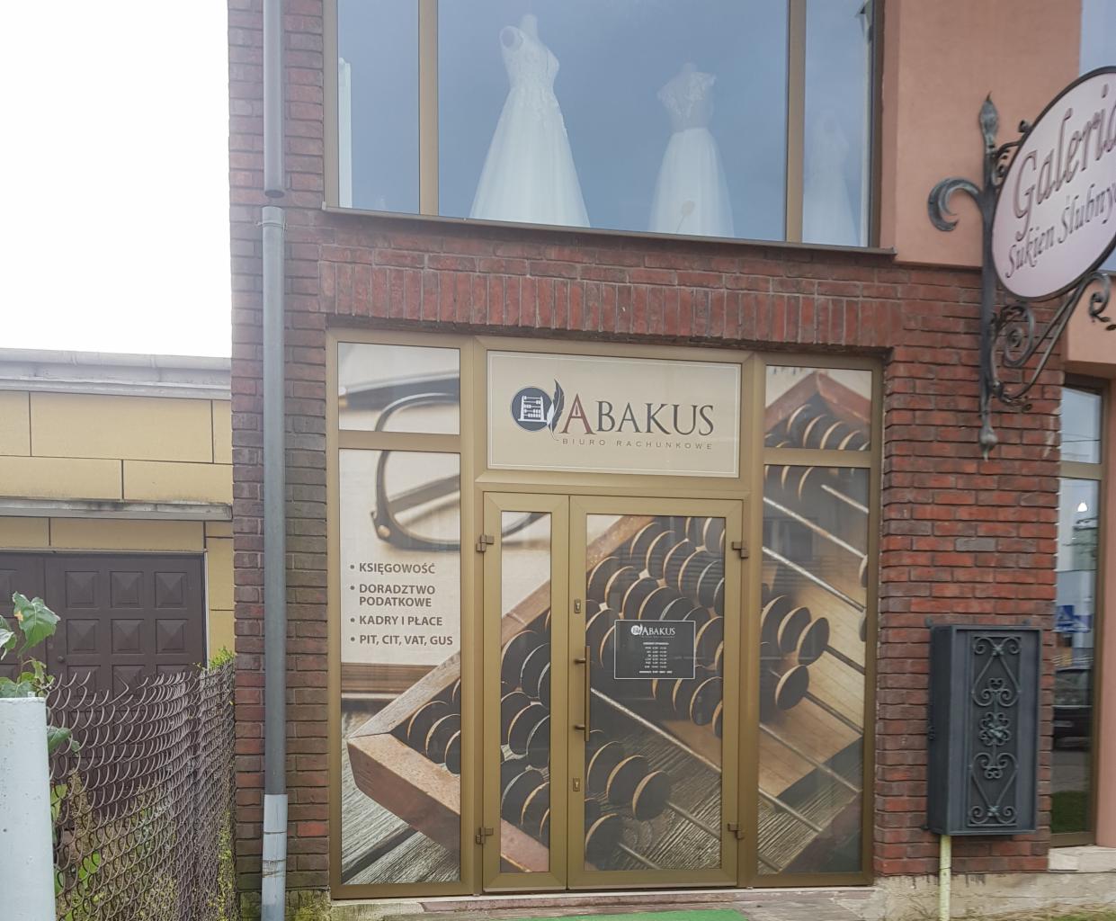 Fasada budynku z szyldem 'ABAKUS BIURO RACHUNKOWE', oklejona grafiką przedstawiającą liczydło i okulary, w oknach widoczne suknie ślubne