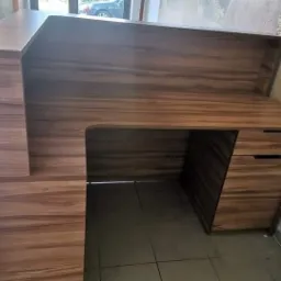 Biurko z drewna o ciepłym odcieniu z szufladami, widoczne z boku, z blatem na dwóch poziomach i oświetleniem naturalnym z okna w tle.