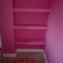 Różowe wnętrze z wnęką i trzema półkami, świeżo pomalowane, widoczne niedoskonałości na podłodze.