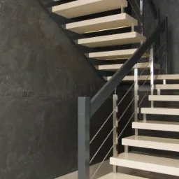 Nowoczesne schody wewnętrzne z metalową balustradą i podświetlanymi stopniami, na tle ściany z efektem betonu.