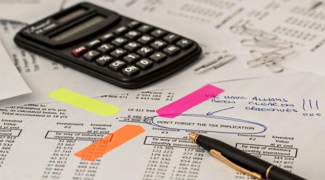 Kalkulator, długopis i kolorowe karteczki na wydruku z danymi finansowymi i notatkami o podatkach.