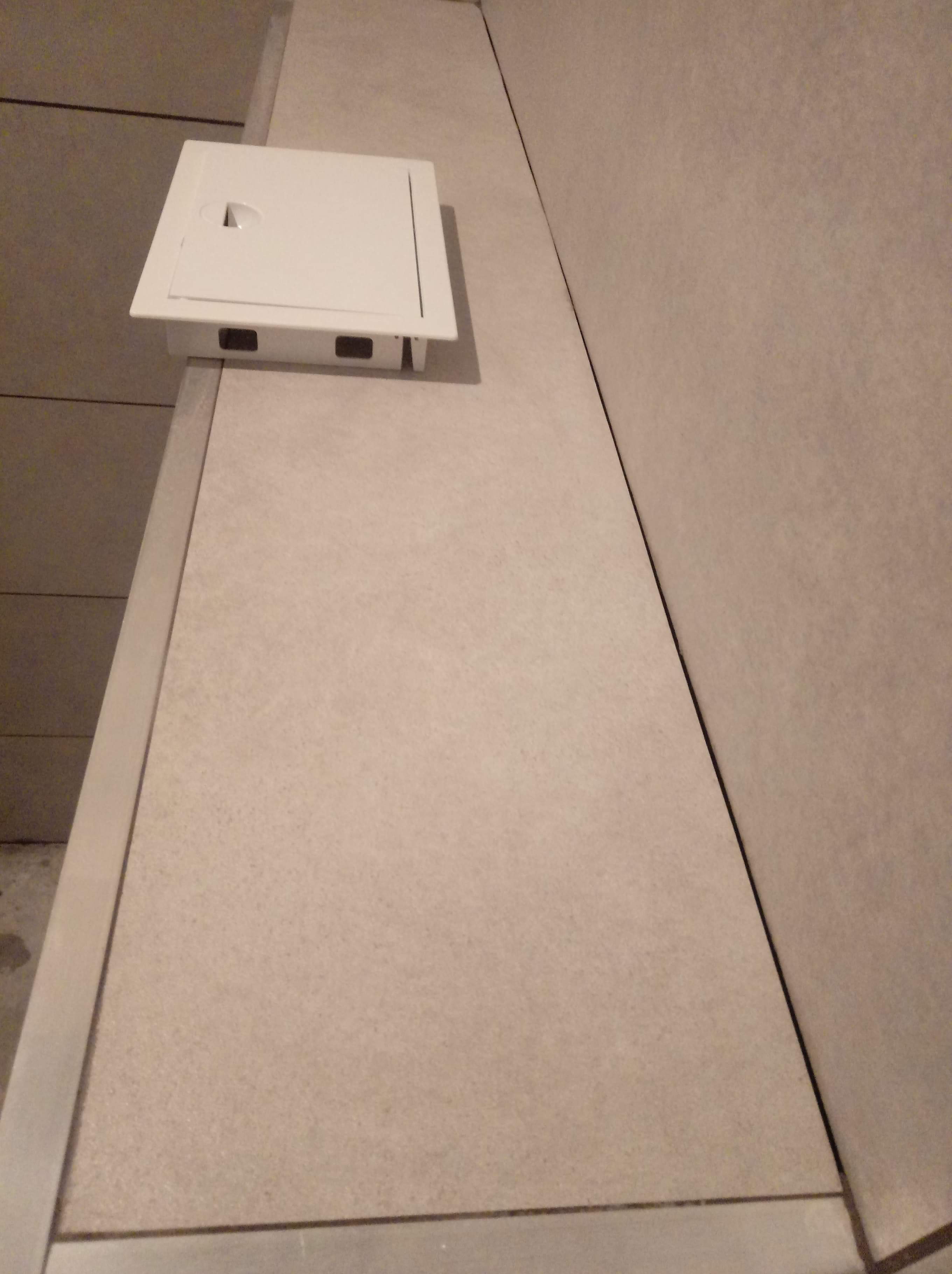 Beżowe płytki na ścianie z ukrytym otworem rewizyjnym zamykanym na biały, kwadratowy właz.