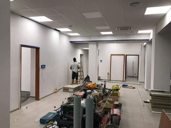 Wnętrze w trakcie remontu: malowanie ścian na biało, widoczne narzędzia, drabina i przygotowane ościeżnice drzwiowe, zabezpieczone taśmą malarską.