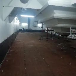 Przygotowanie podłoża z siatką zbrojeniową i dystansami pod wylewkę w pomieszczeniu przemysłowym, pracownik w oddali używa maszyny do wyrównywania powierzchni.