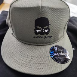 NITKA DAWID KOMARNICKI - Szara czapka typu snapback z czarnym nadrukiem czaszki w masce gazowej i napisem 'Full Car Garage', obok naklejka 'The Original Snapback'.