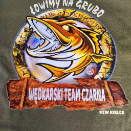 Zielona koszulka z nadrukiem przedstawiającym stylizowaną rybę z otwartą paszczą i napisem 'Łowimy na grubo', poniżej napis 'Wędkarski Team Czarna' na tle imitującym drewnianą tabliczkę, oraz 'PZW...