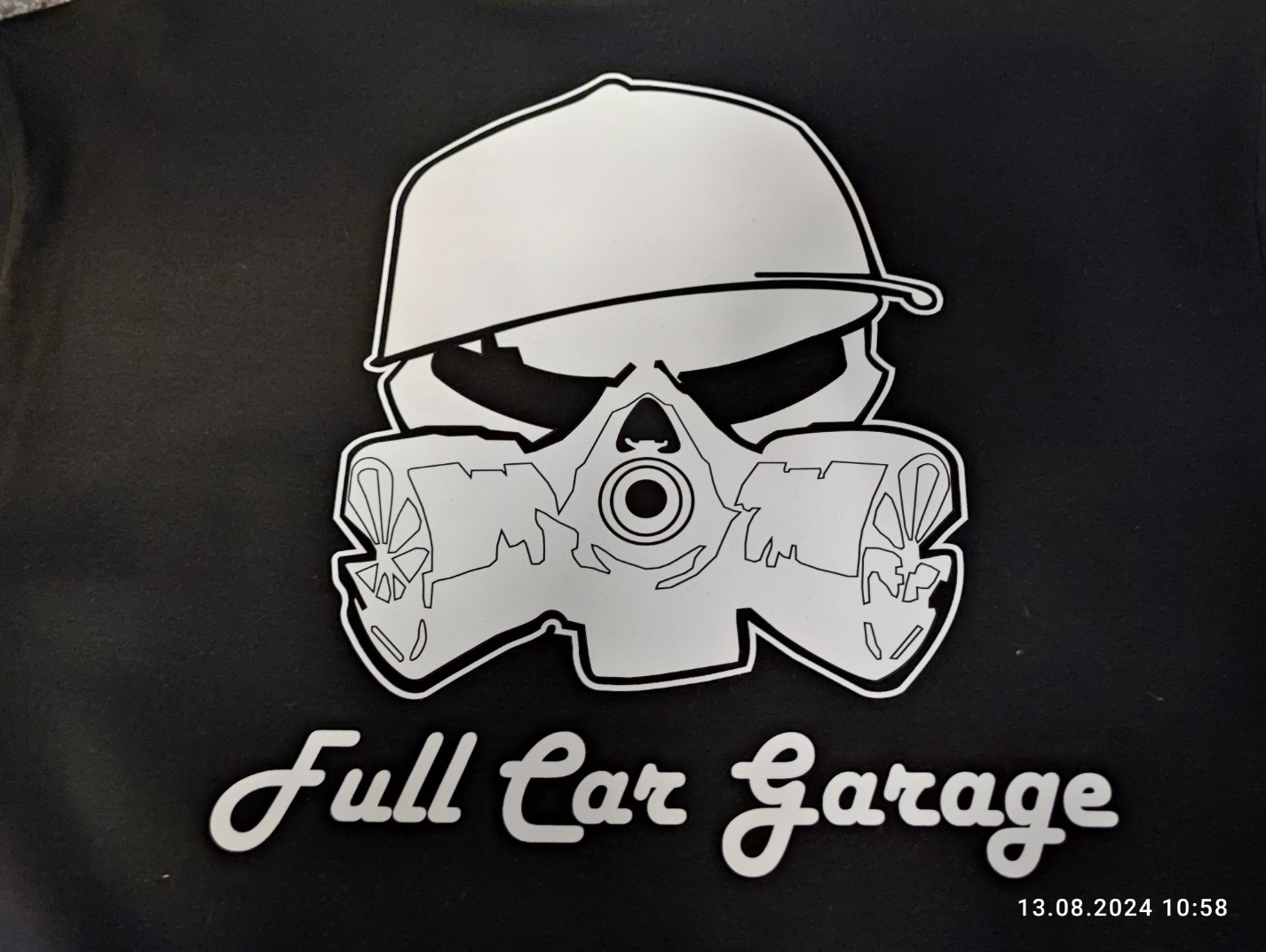 Czarna koszulka z białym nadrukiem przedstawiającym czaszkę w czapce i masce gazowej z napisem 'Full Car Garage'.