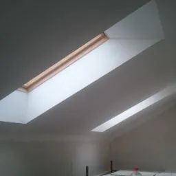 Poddasze w trakcie remontu z dwoma oknami dachowymi, widoczne rusztowanie i butelka Capri-Sonne na desce.