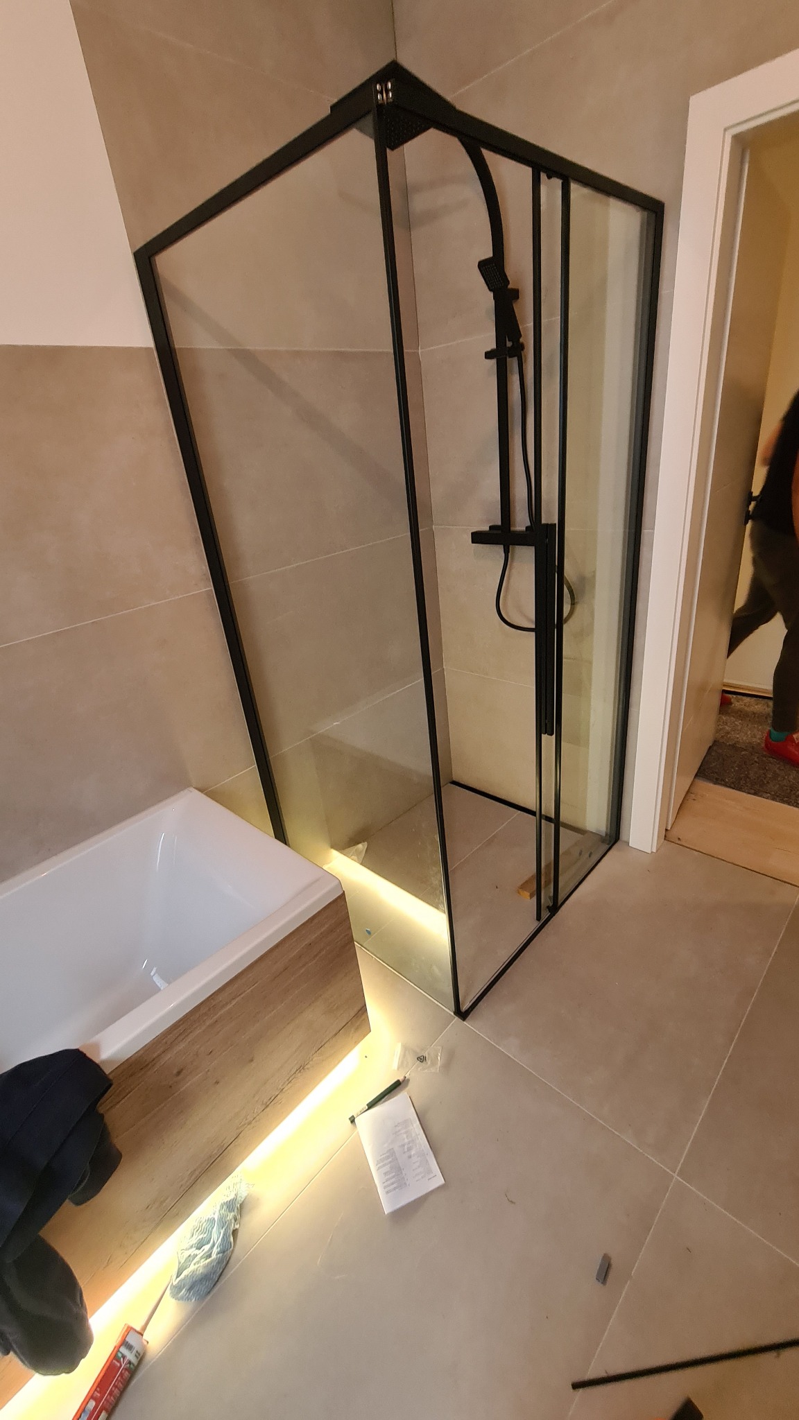 Montaż kabiny prysznicowej z czarnymi profilami w nowoczesnej łazience z podświetleniem LED wanny, widoczne narzędzia i instrukcja.