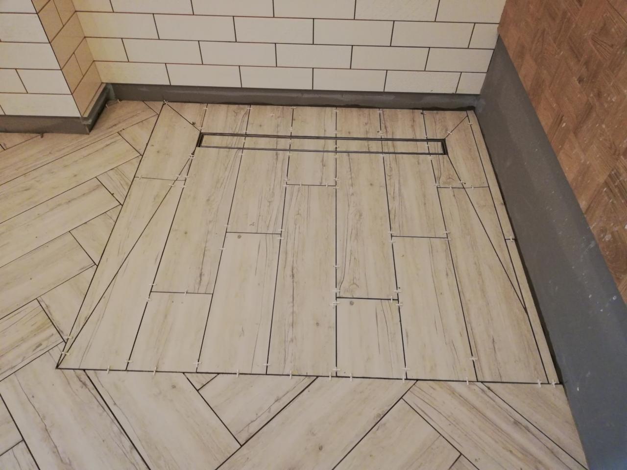 Układanie podłogi z płytek imitujących drewno w Pogórzu, widoczny odpływ liniowy i krzyżyki dystansowe.