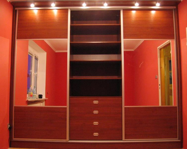 Wnętrze z zabudowaną szafą przesuwną z lustrami i otwartymi półkami w odcieniach brązu, oświetlenie punktowe na górze, widok na pokój z czerwonymi ścianami w odbiciu lustrzanym.