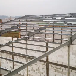 Budowa domu: ściany z białych bloczków i stalowa konstrukcja dachu w trakcie montażu, widok z góry.