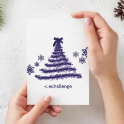 Dwie dłonie trzymają kartkę świąteczną z motywem choinki i płatków śniegu w odcieniach fioletu, widoczny napis 'echallenge', w tle gałązka świerku i szyszka na białym tle.