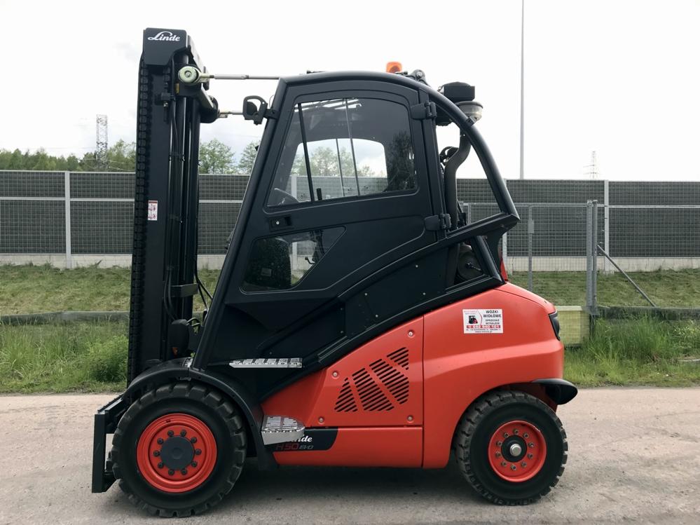 Pomarańczowo-czarny wózek widłowy Linde H50D na zewnątrz, widok z boku, z naklejką informacyjną na karoserii. Na drugim planie siatka zabezpieczająca.