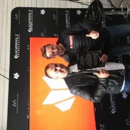 Dwóch mężczyzn pozuje na tle ścianki z logo Blachprofil 2, trzymając certyfikaty i pokazując kciuki w górę.