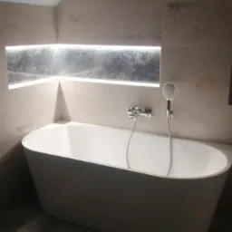 Nowoczesna łazienka w odcieniach szarości z wolnostojącą białą wanną, podświetlaną wnęką i minimalistyczną armaturą.