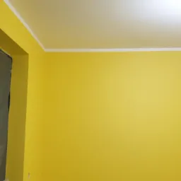 Żółta ściana po malowaniu, z zabezpieczonym folią oknem, widoczne białe listwy sufitowe.