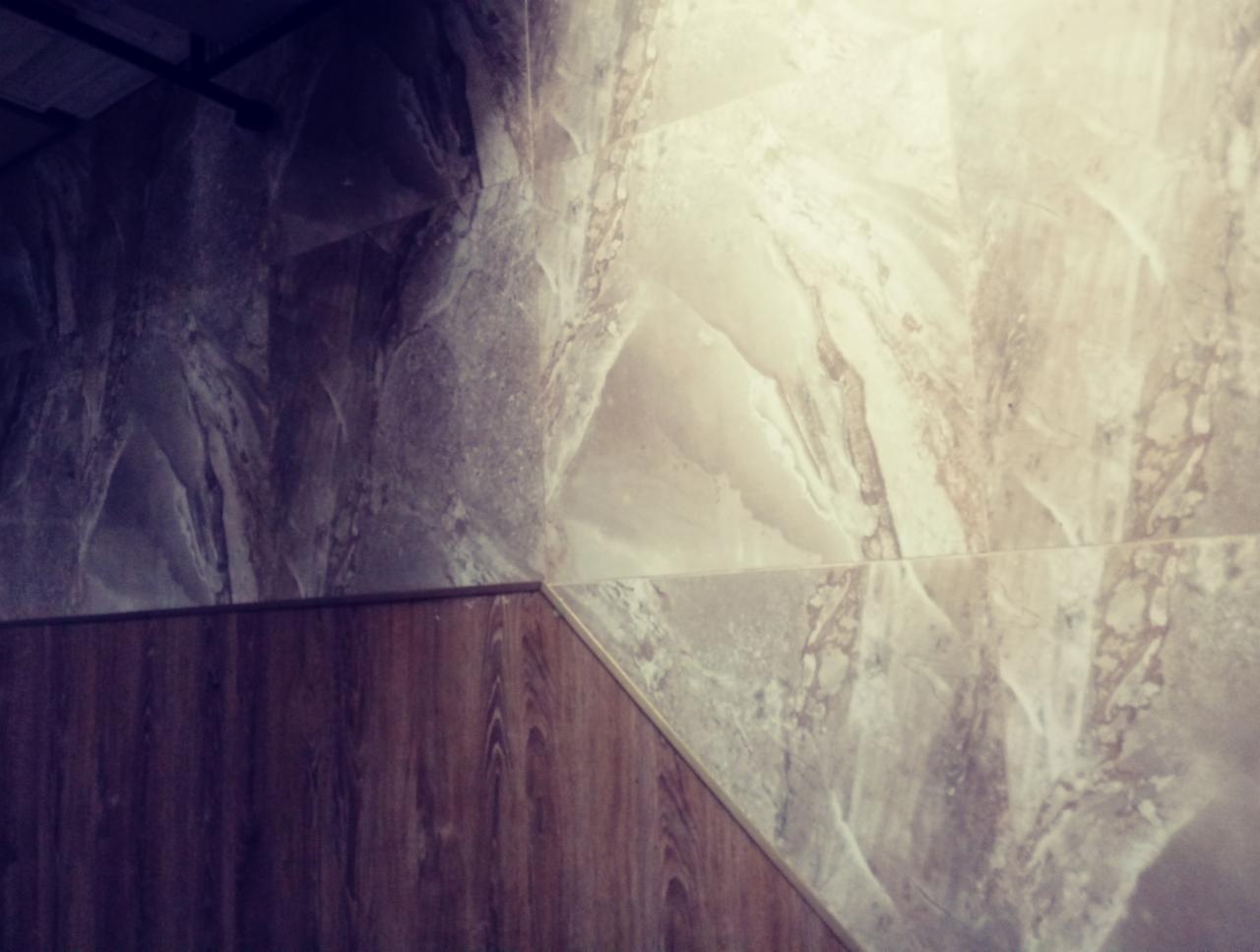 Wykończenie ściany płytkami imitującymi marmur w Zgierzu, z widocznym połączeniem z panelami drewnopodobnymi na dole.