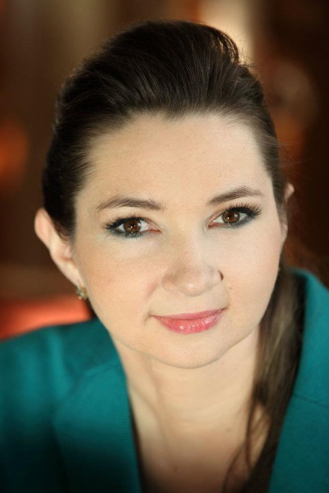 Portret kobiety z delikatnym uśmiechem, brązowymi oczami i zielonym cieniem na powiekach, ubrana w turkusową bluzkę.