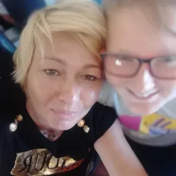 Selfie dwóch uśmiechniętych kobiet, jedna z krótkimi blond włosami i czarnej koszulce, druga w okularach. Nieostre tło.