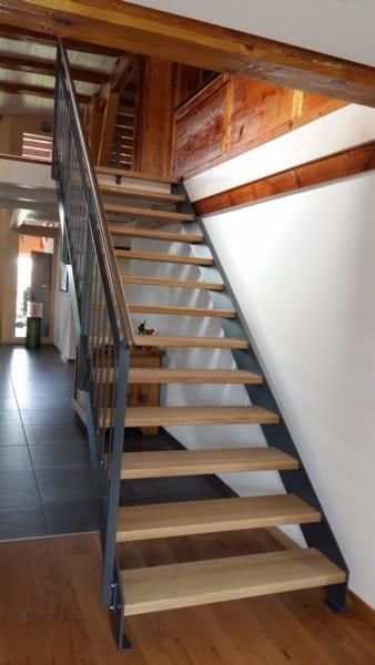 Nowoczesne schody z metalową konstrukcją i drewnianymi stopniami, widok z dołu, z elementami drewnianej konstrukcji dachu w tle.