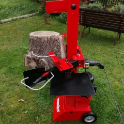 Czerwona, elektryczna łuparka do drewna marki Hectory ustawiona na trawie obok pniaka.