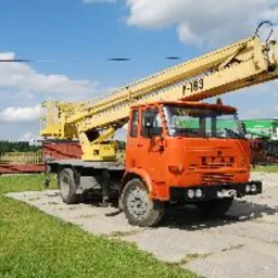 Pomarańczowy samochód ciężarowy Star z żółtym podnośnikiem koszowym na betonowym placu, widoczny numer F-163 na koszu, w tle ogrodzenie i zieleń.